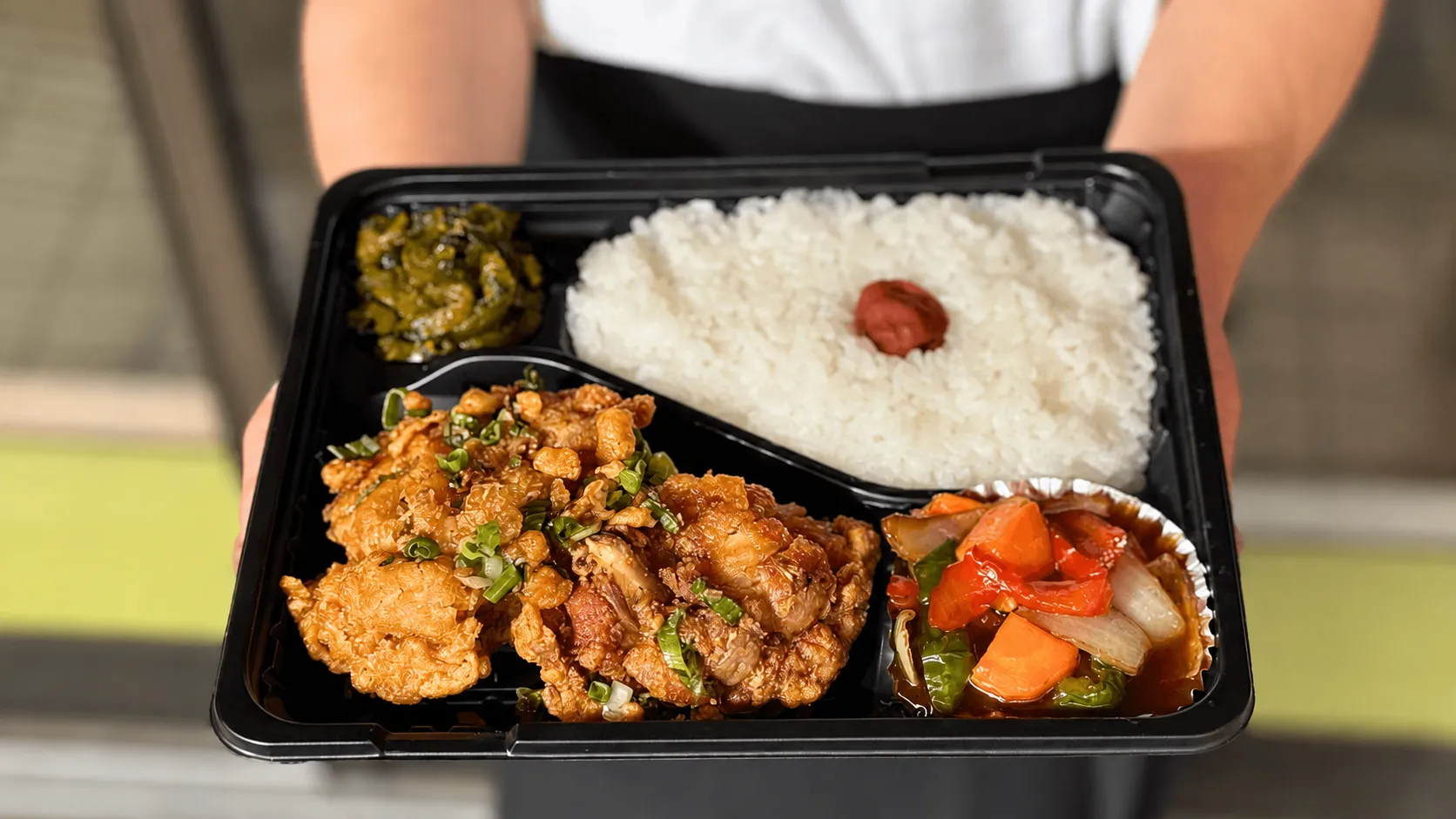 有田・上海飯店の唐揚げ弁当。唐揚げ、ご飯、彩り野菜の餡かけ、高菜を詰めた黒い容器